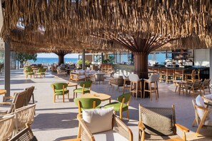 An outdoor seating area with wicker chairs and tables, a bar, and a view of the sea. - Paralos Kosta Alímia (Hersonissos)