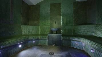 Un spa con paredes de mosaico verde, una fuente de piedra central y suelo de baldosas.