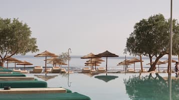 Zona de piscina con sillas de descanso y sombrillas, con vista al mar.