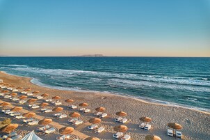 A beach with rows of sun loungers and umbrellas, a clear sky, and the ocean.