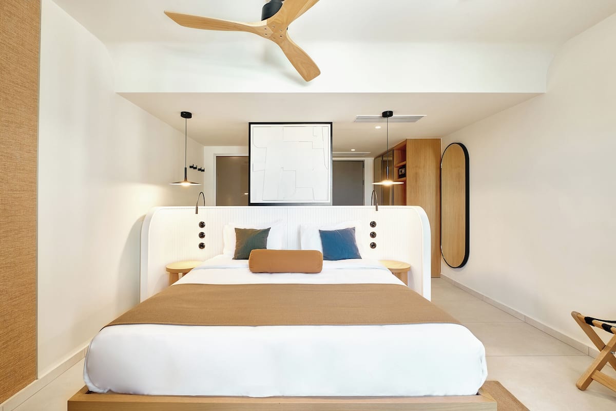A modern bedroom with a large bed, a ceiling fan, and a view of the bathroom.