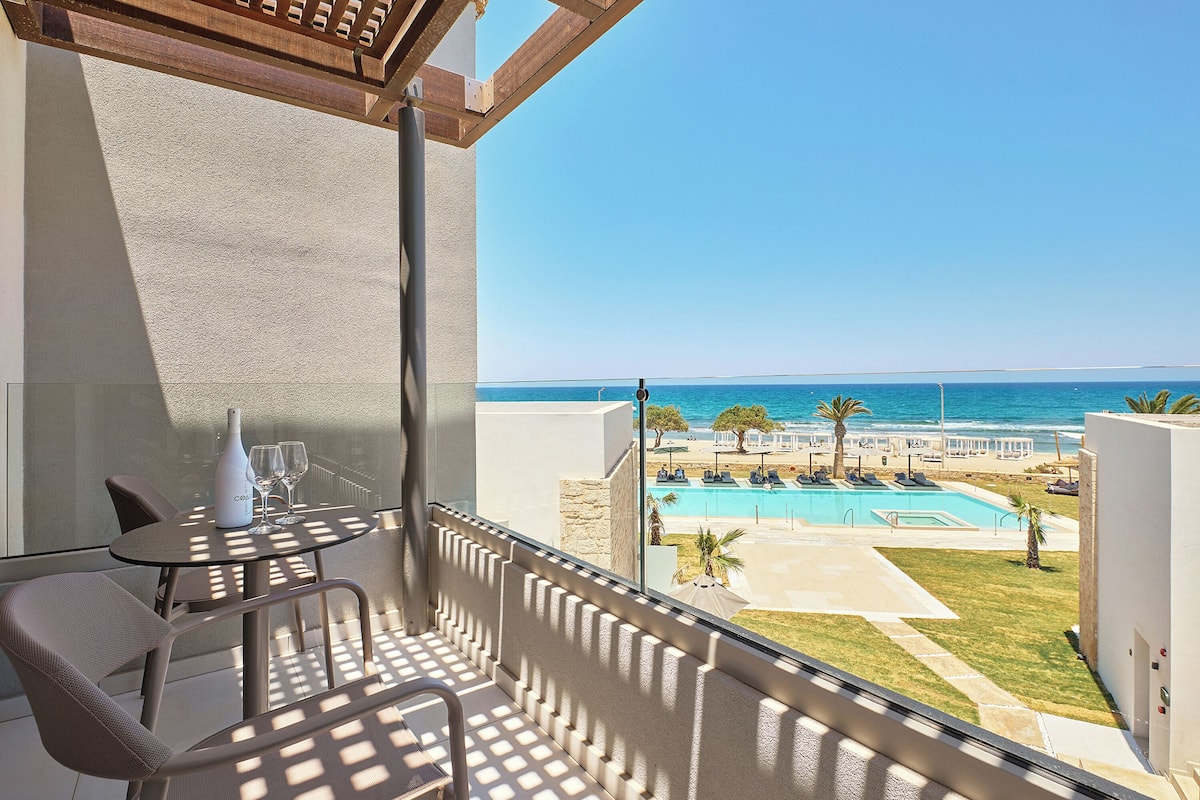 A balcony with a table and chairs, overlooking a pool and beach area.