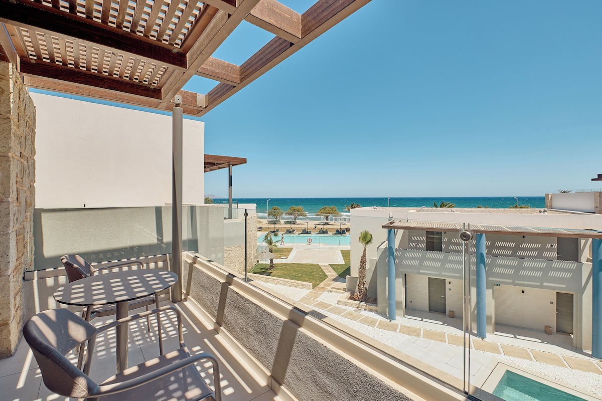 A balcony with a table and chairs, overlooking a pool and a clear blue sky.