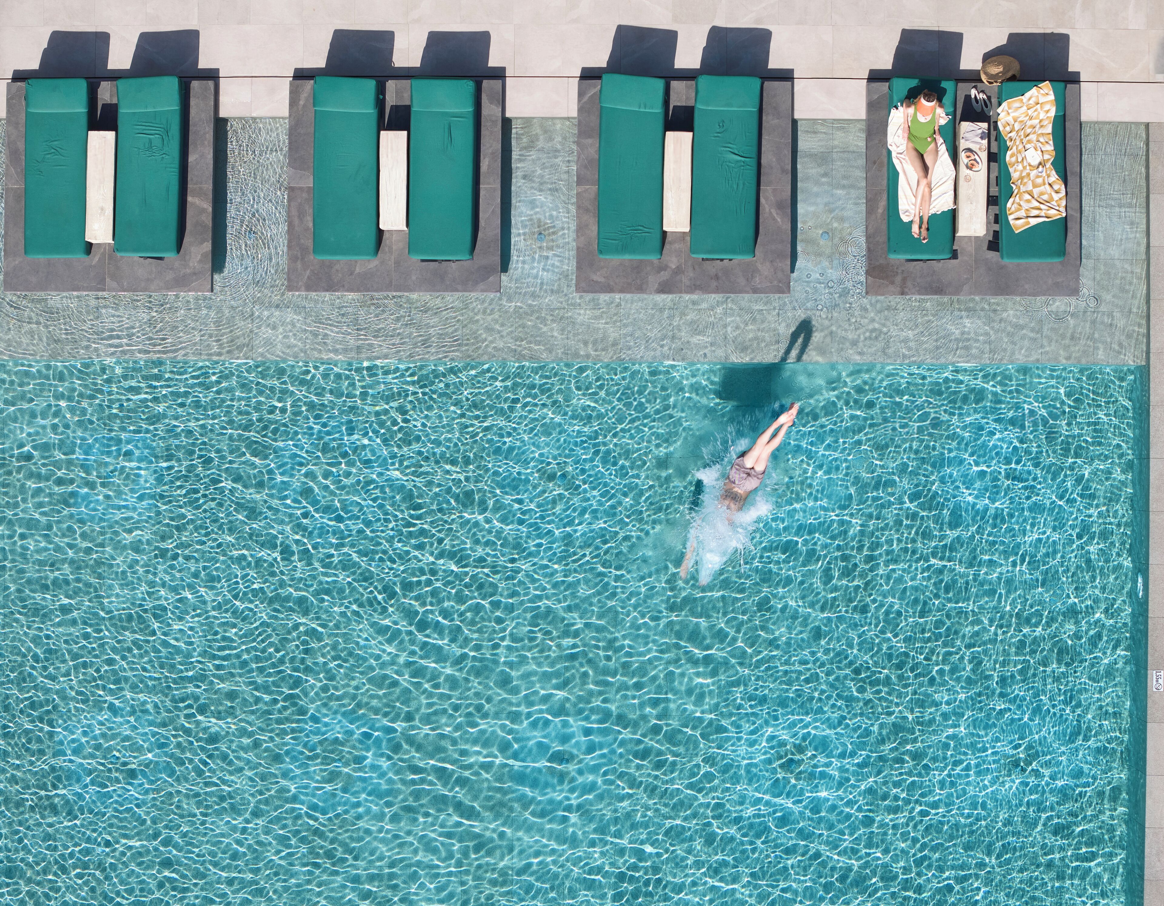 Vista aérea de una piscina con múltiples sillas de descanso y una persona nadando.