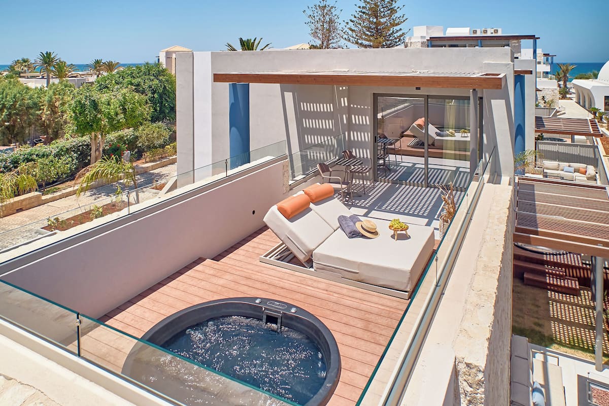 A rooftop terrace with a hot tub, lounge chairs, and a glass balustrade overlooking a coastal area.