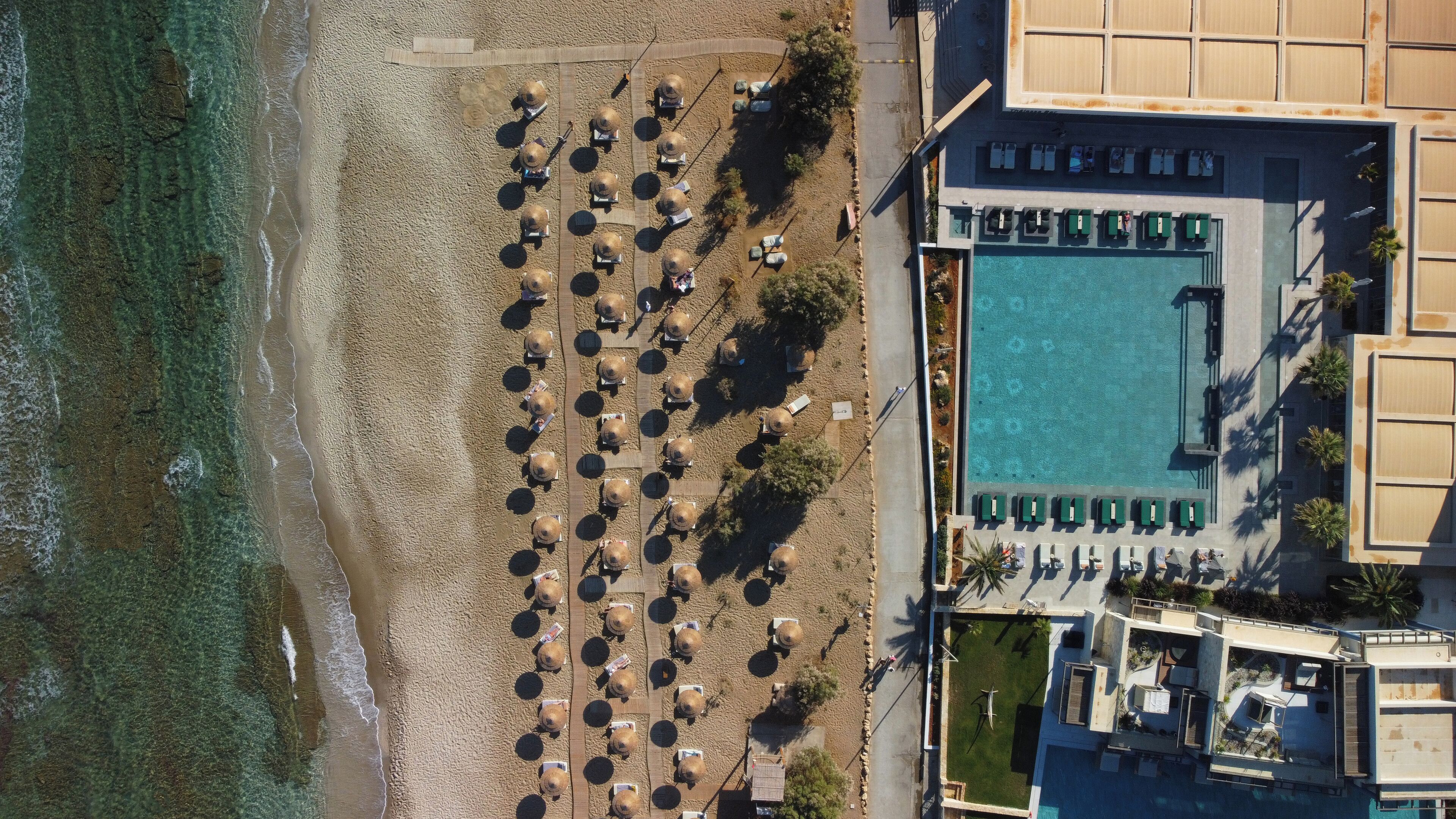 An aerial view of a beachside hotel with a swimming pool, sun loungers, and a boardwalk.