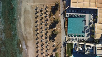 An aerial view of a beachside hotel with a swimming pool, sun loungers, and a boardwalk.