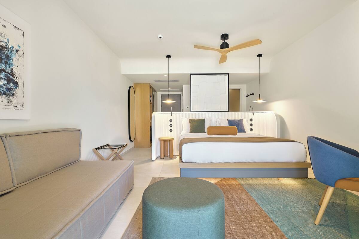 A modern bedroom with a bed, a sofa, a chair, and a ceiling fan.