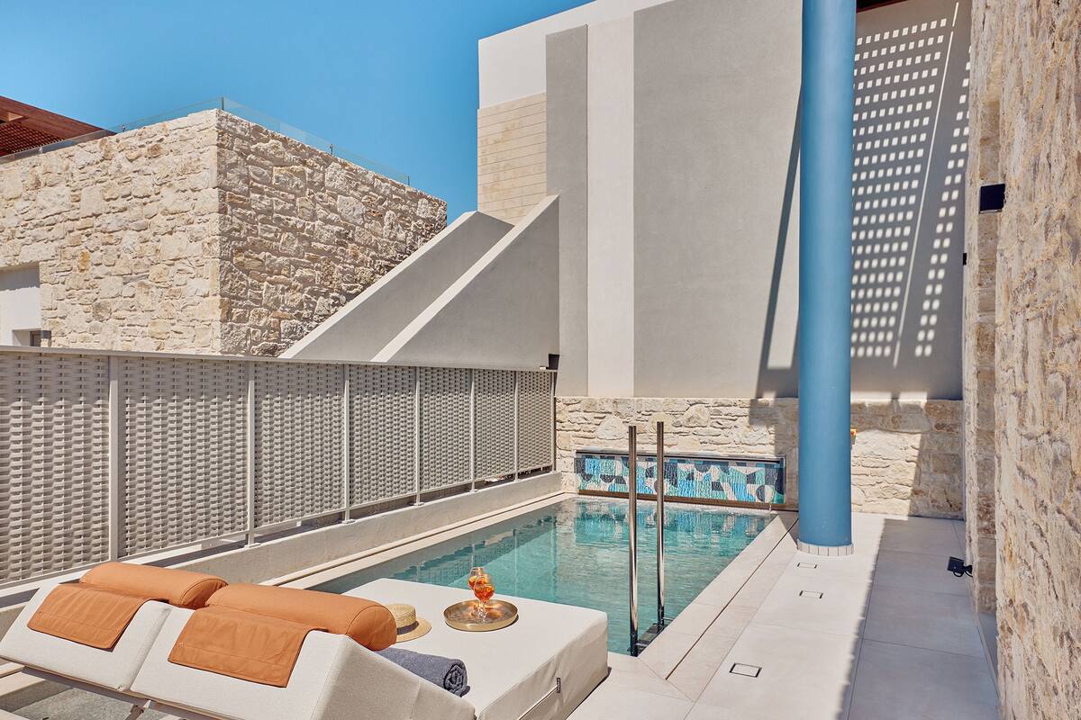 A rooftop pool area with lounge chairs, a glass of wine, and a stone wall.