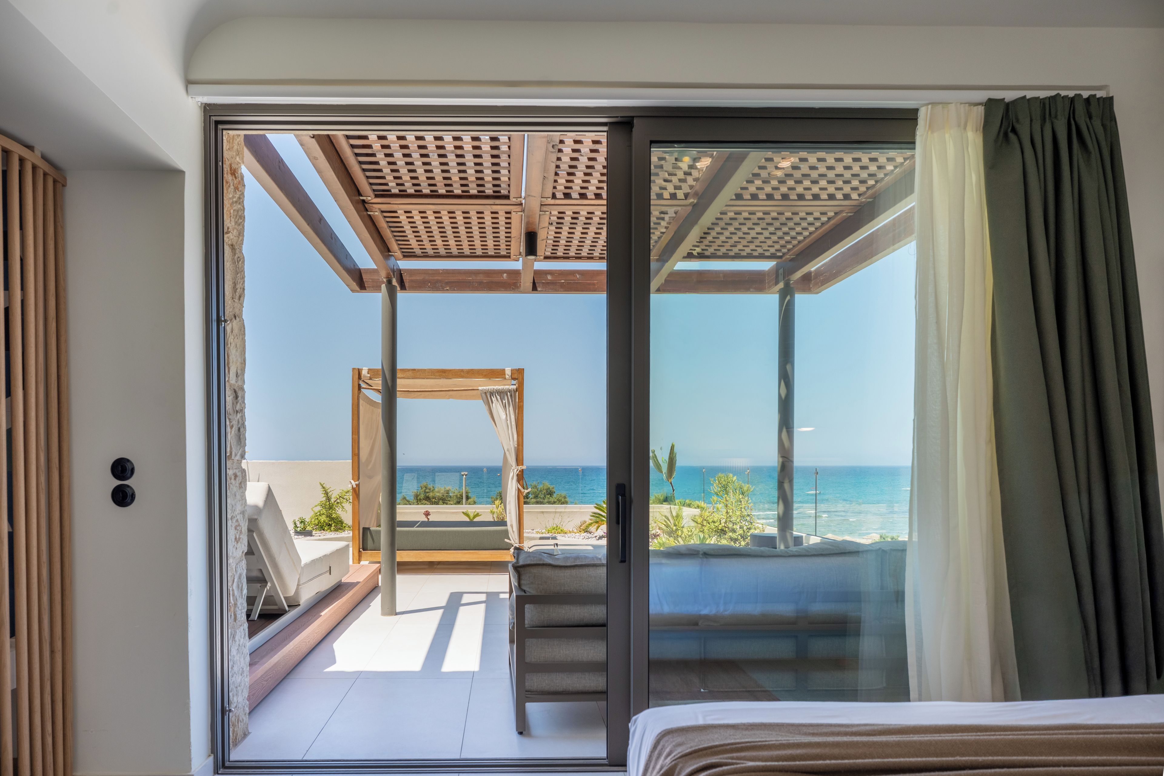Una habitación con cama, puerta corrediza de vidrio que da a un balcón con vista al mar.