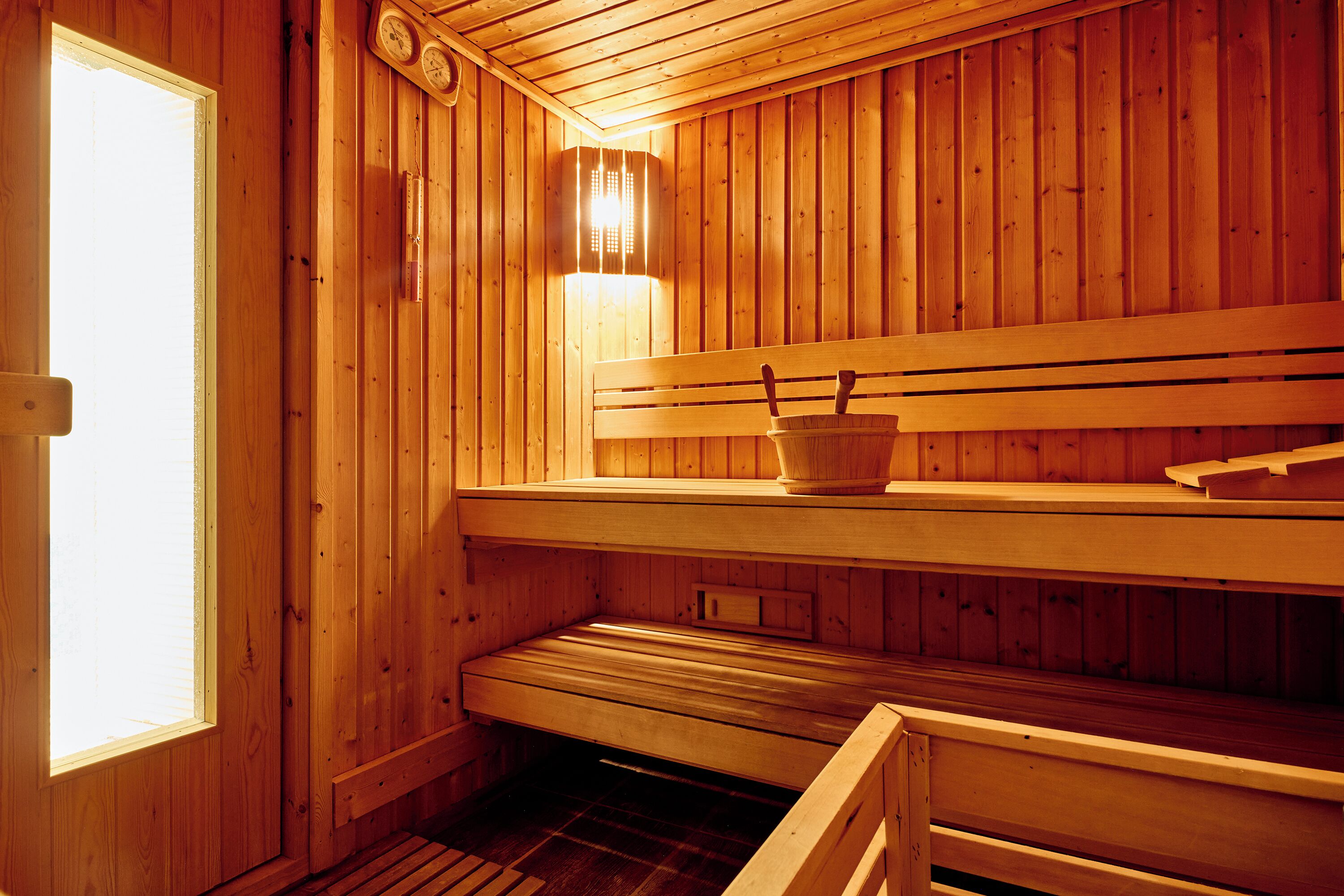 A wooden sauna with benches and a bench seat, a wall-mounted heater, and a window.