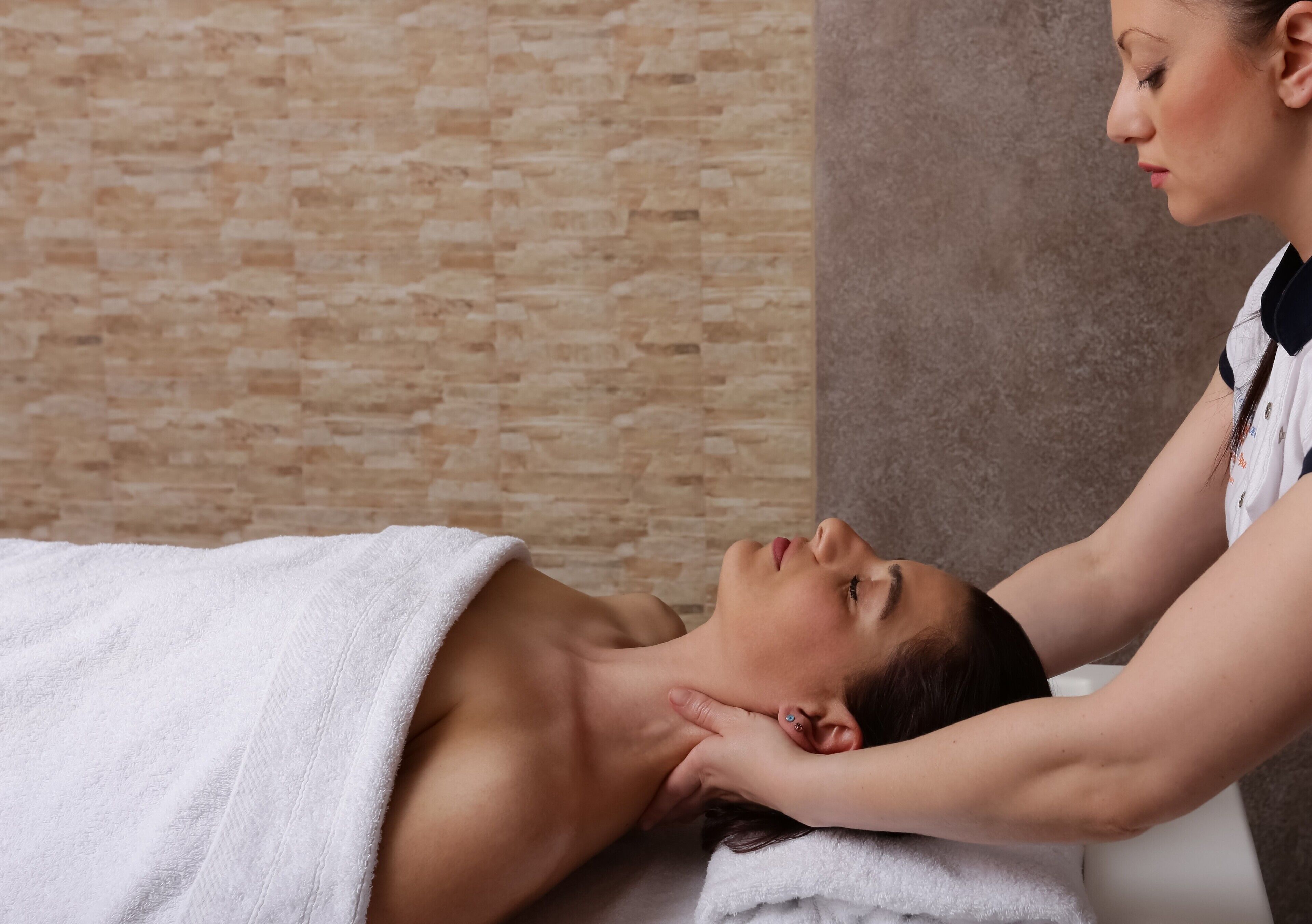 Une personne reçoit un massage du cou dans un spa, avec un mur de pierres en arrière-plan.