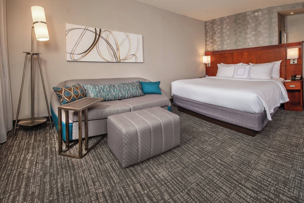 Ein Hotelzimmer mit einem großen Bett, einer Couch mit gemusterten Kissen, einem kleinen Tisch und einer Stehlampe.