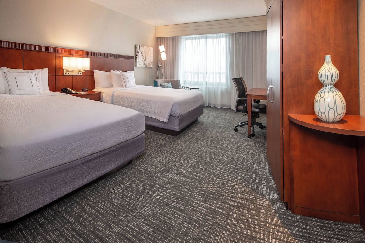 Ein Hotelzimmer mit zwei Betten, einem Schreibtisch, einem Stuhl, einer Lampe und einer Vase.