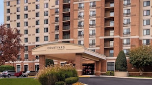L’entrée d’un hôtel Courtyard by Marriott, avec une façade en briques, de nombreux balcons et une allée couverte.