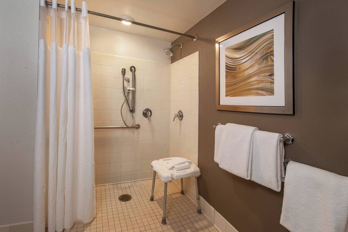 Ein modernes Badezimmer mit Dusche, einem kleinen Hocker mit Handtüchern und einem gerahmten Kunstwerk an der Wand.