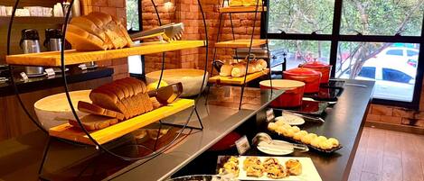 A breakfast buffet with various breads and pastries displayed on shelves and a large glass bowl of dessert.