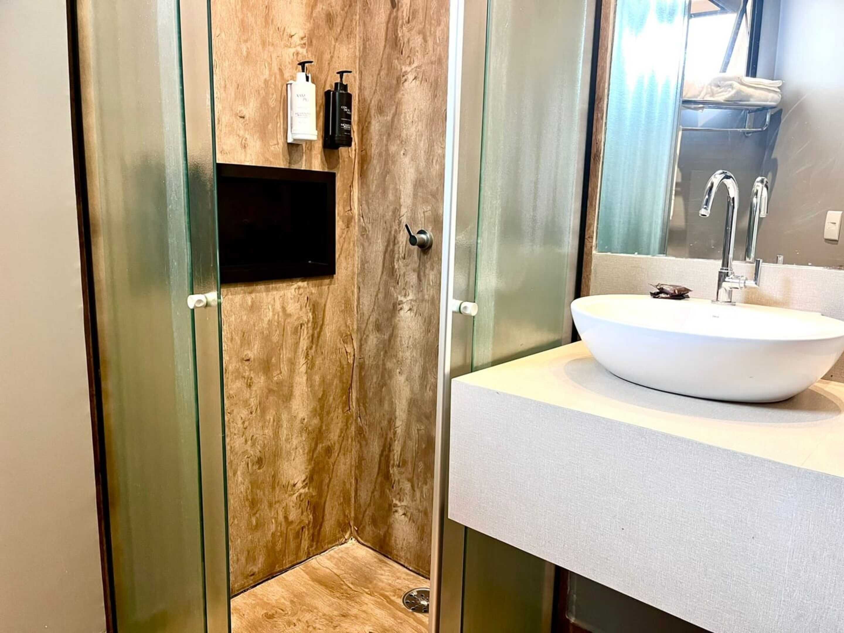 A modern bathroom with a large mirror, a white sink, and a wooden wall.
