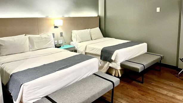 A hotel room with two beds, a nightstand, a lamp, and a bench. - Oasis Plaza Hotel (Ribeirão Preto)