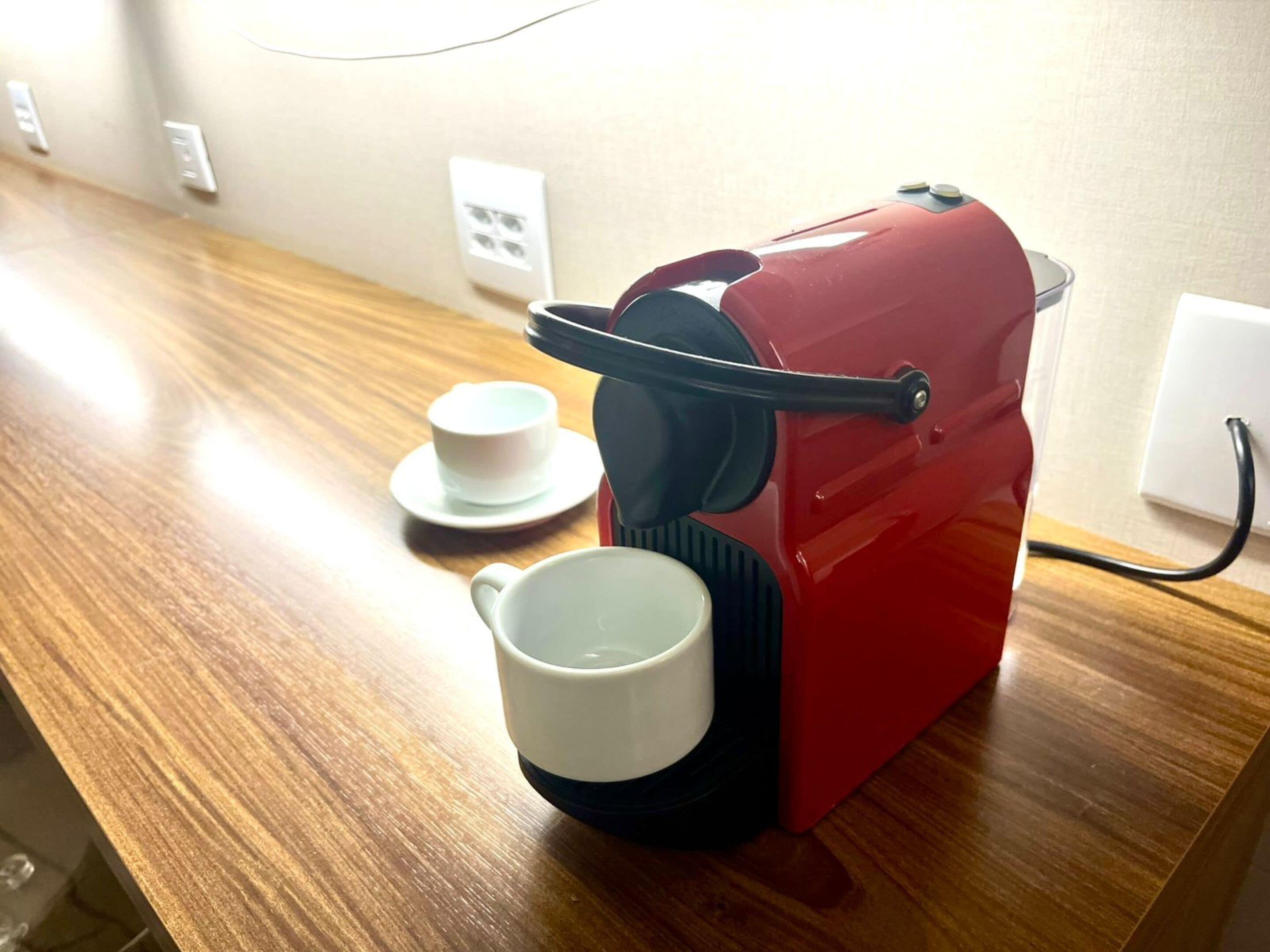 A red coffee machine with a cup and saucer on a wooden table.