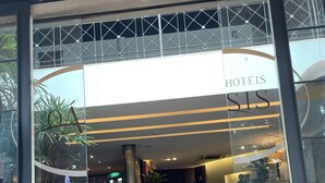 Een hotelentree met een receptiebalie, een glazen deur en een bord met de tekst 'HOTÉIS SIS'.