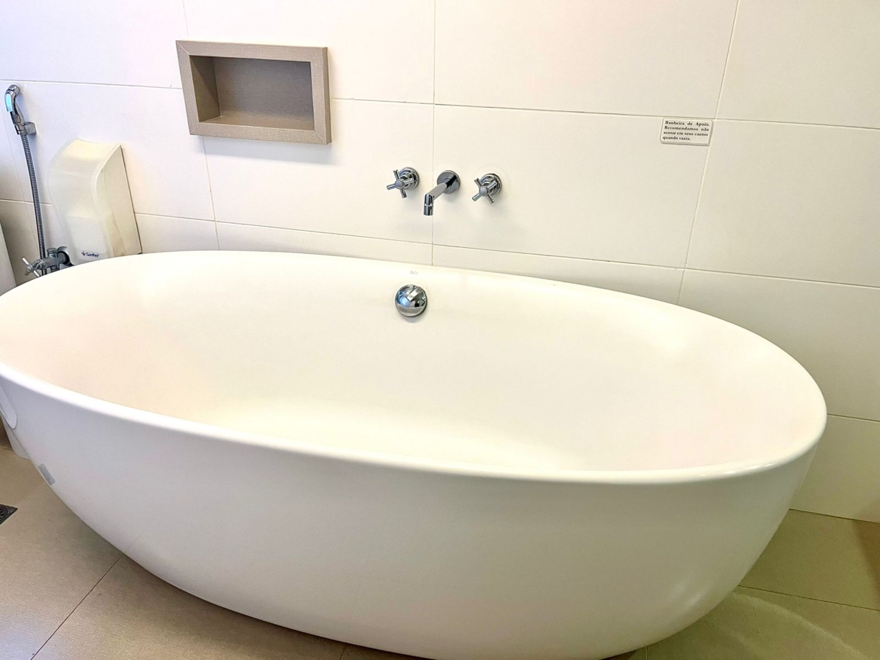 A white bathtub with a single faucet, a soap dispenser, and a small wooden shelf above it.