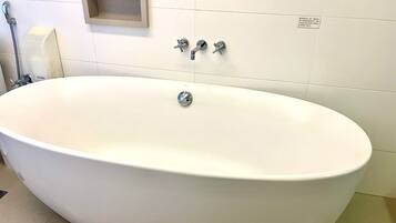 A white bathtub with a single faucet, a soap dispenser, and a small wooden shelf above it.