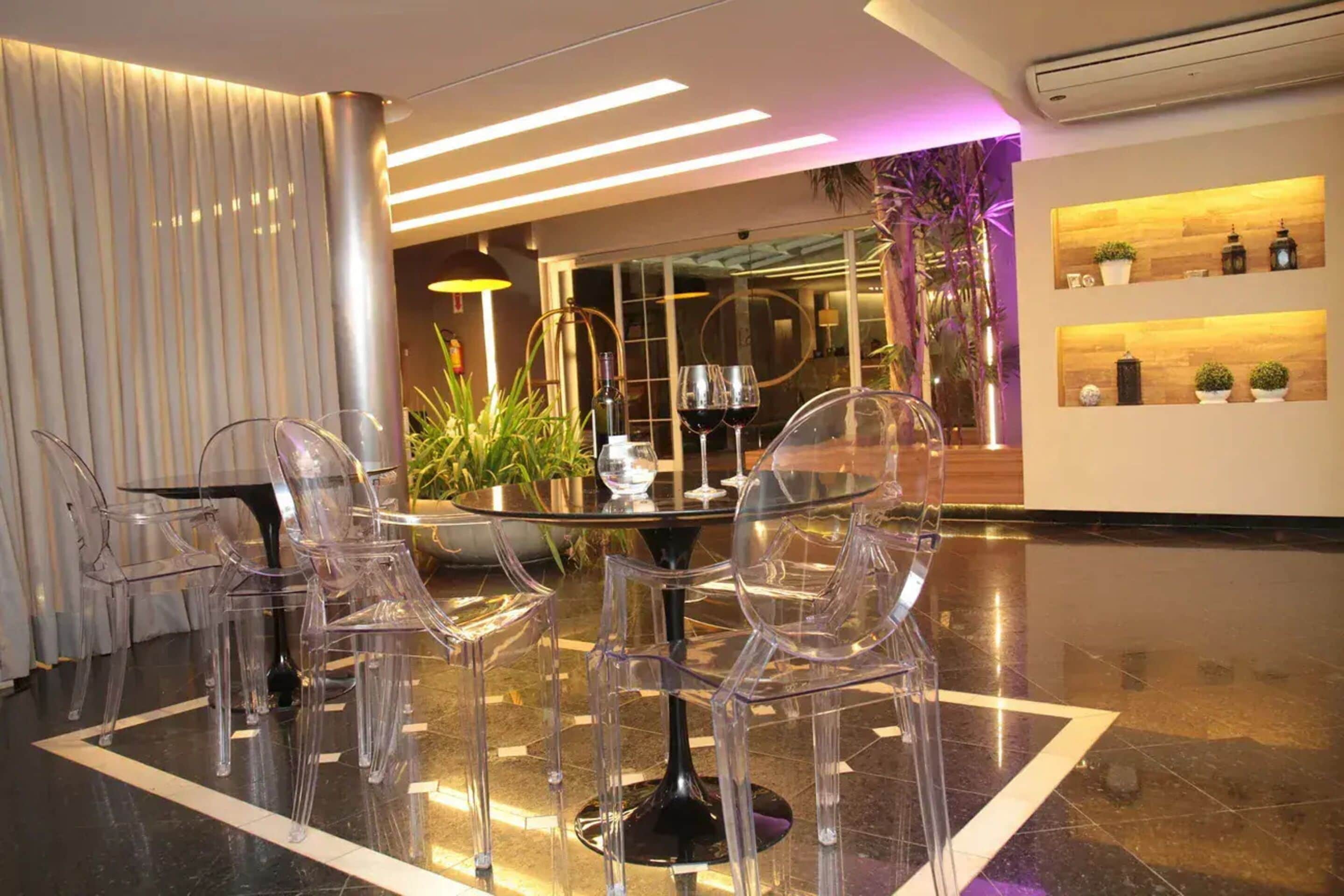 Un interior moderno con una mesa de vidrio rodeada de sillas transparentes, una planta en maceta y un estante de madera con objetos decorativos.