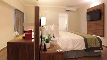 Quarto de hotel com cama, escrivaninha, cadeira, TV fixada na parede e aparelho de ar condicionado.