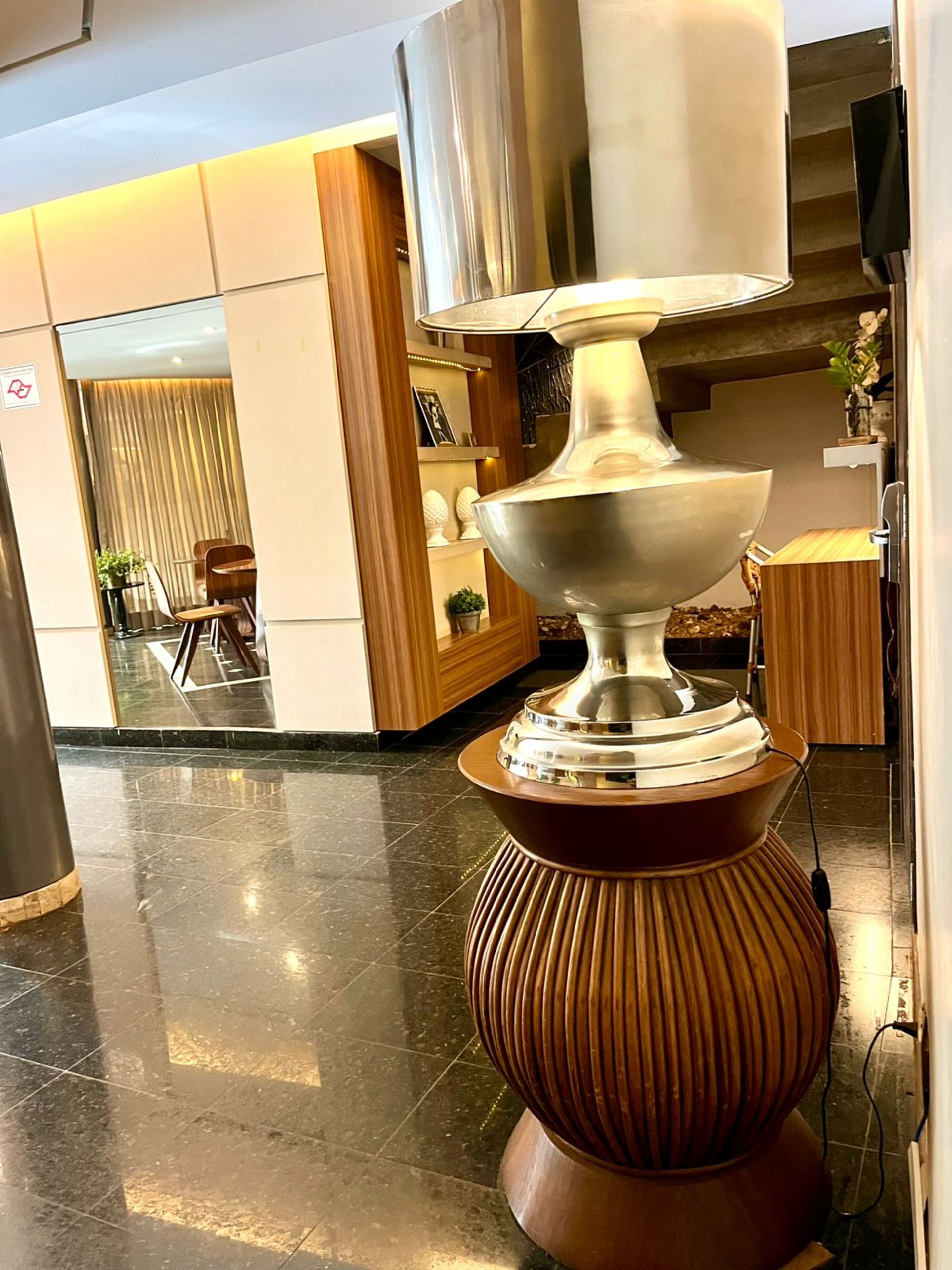 A modern lobby with a large, metallic, sculptural light fixture on a wooden pedestal.