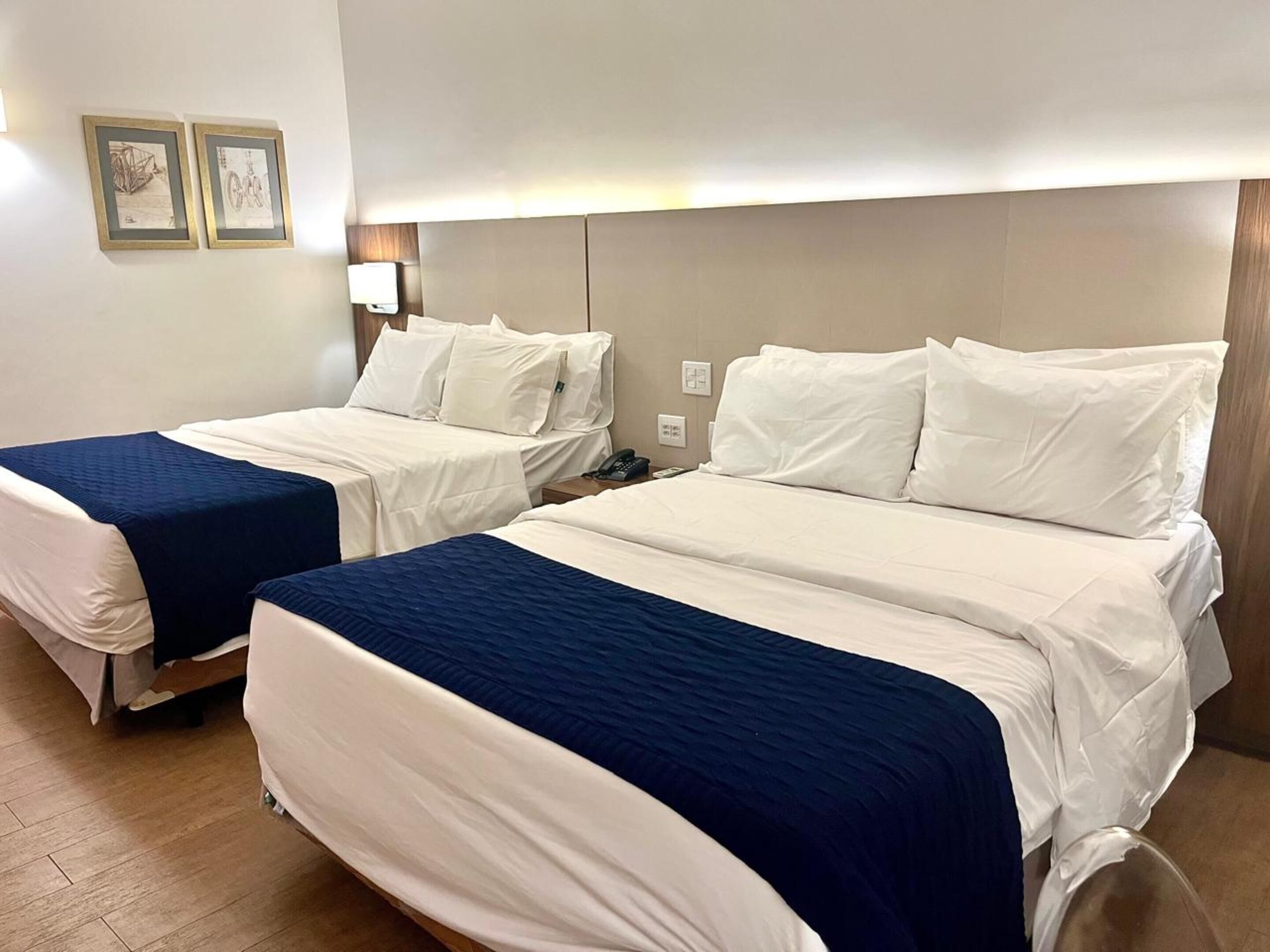 Twee eenpersoonsbedden met wit en blauw beddengoed, een nachtkastje met een lamp en een wandlamp.