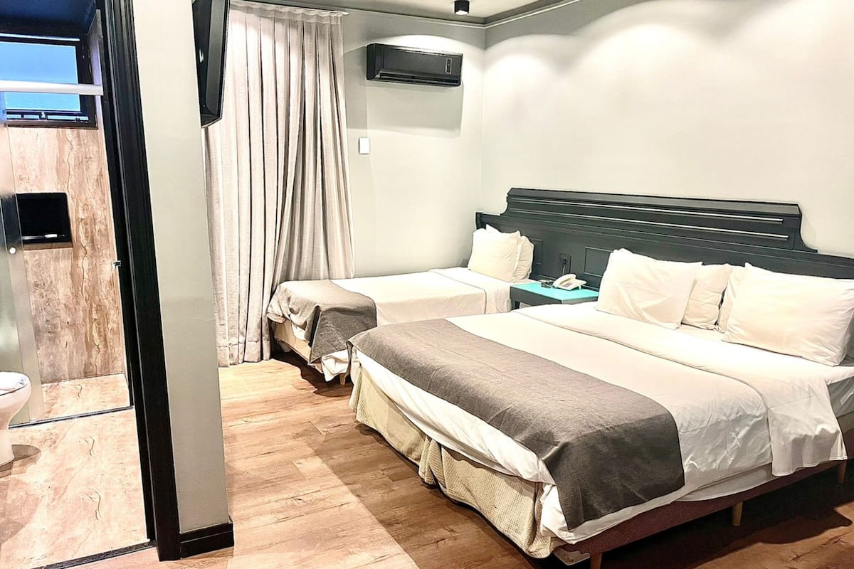 A hotel room with a bed, bedside table, and an air conditioning unit.