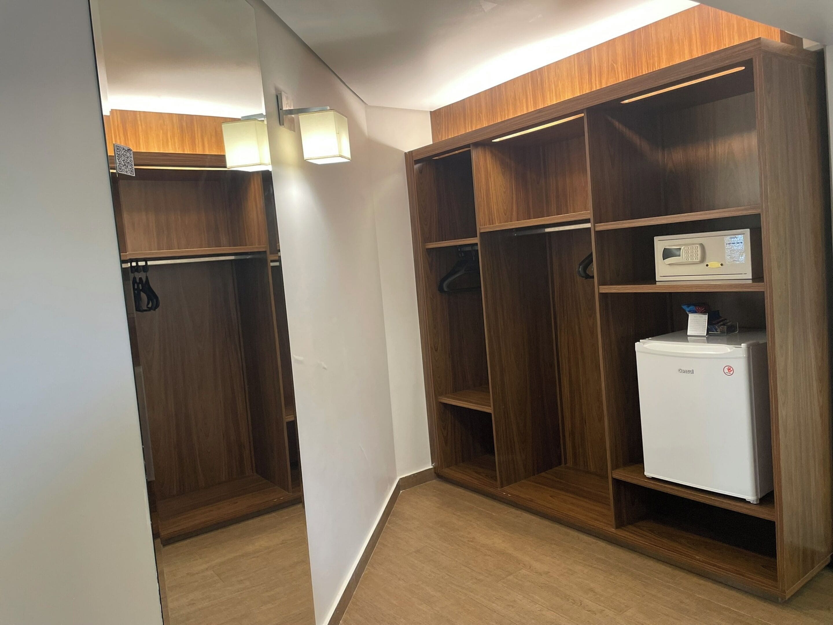 A walk-in closet with wooden shelving, a white refrigerator, and a hanging garment rack.