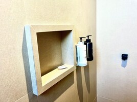 Un baño con estante empotrado, dos dispensadores de jabón para manos y un perchero para toallas.