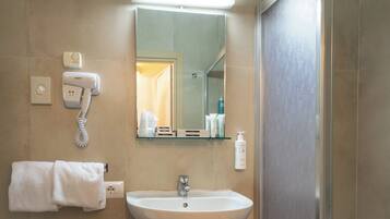 Une salle de bain avec un lavabo blanc, un miroir, un porte-serviettes, un sèche-cheveux et un espace douche.
