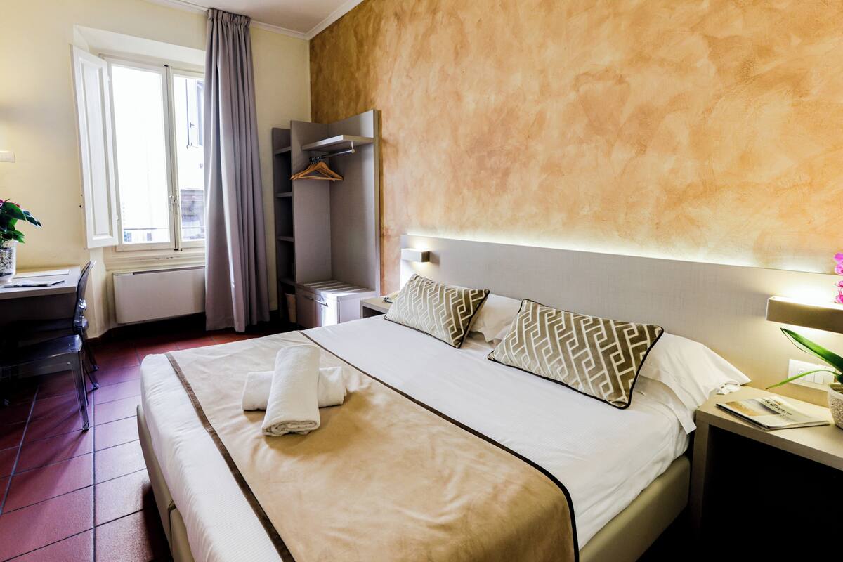 Une chambre d’hôtel avec un grand lit, un bureau, une chaise, une armoire et une fenêtre avec des rideaux.