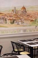 A dining area with tables and chairs, a mural of a cityscape, and a view of a river.