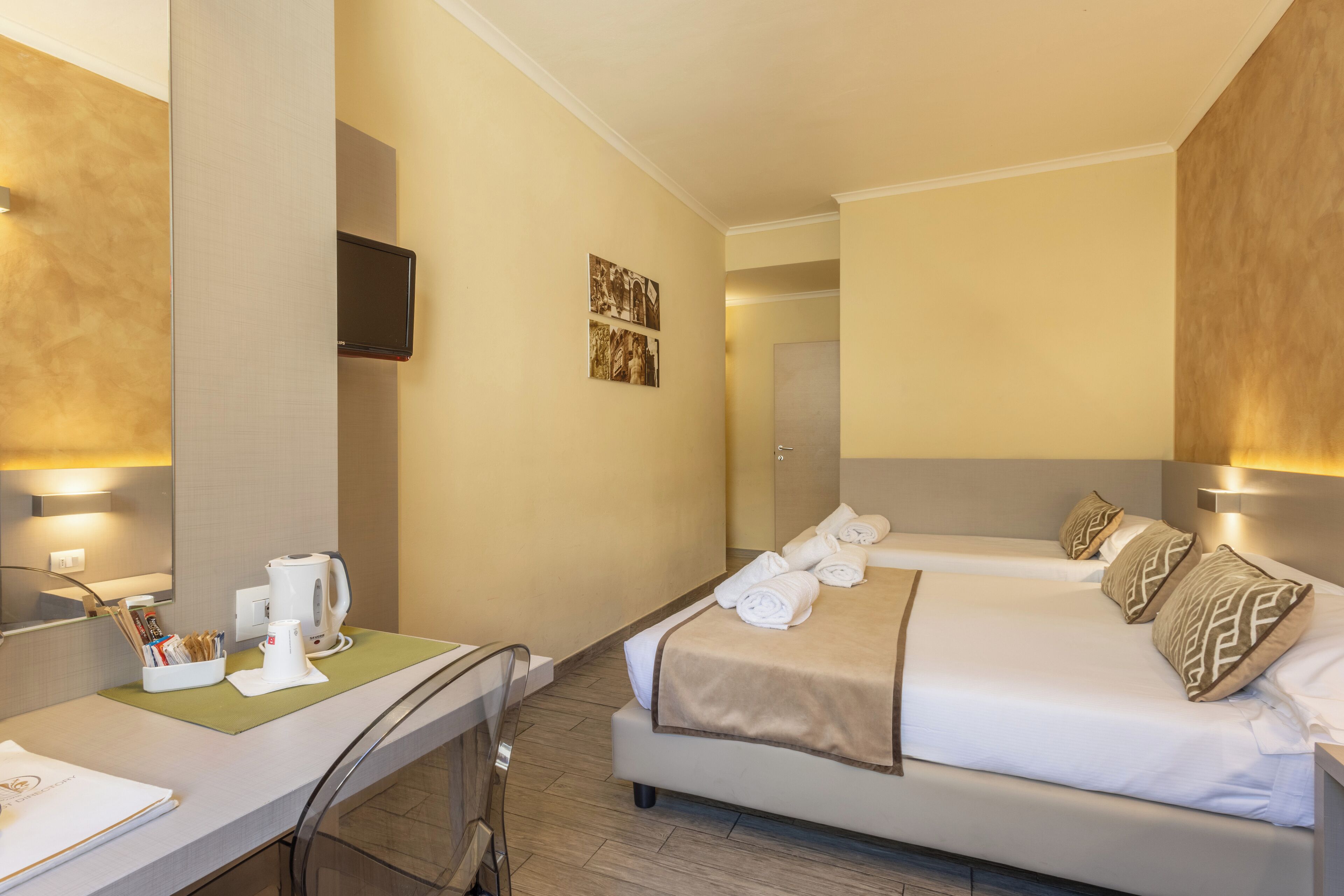 A hotel room with two beds, a desk, a mirror, and a television.