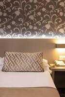 Une chambre d’hôtel avec un papier peint à motifs, un lit avec un oreiller à motifs, une table de chevet avec une lampe et un téléphone.