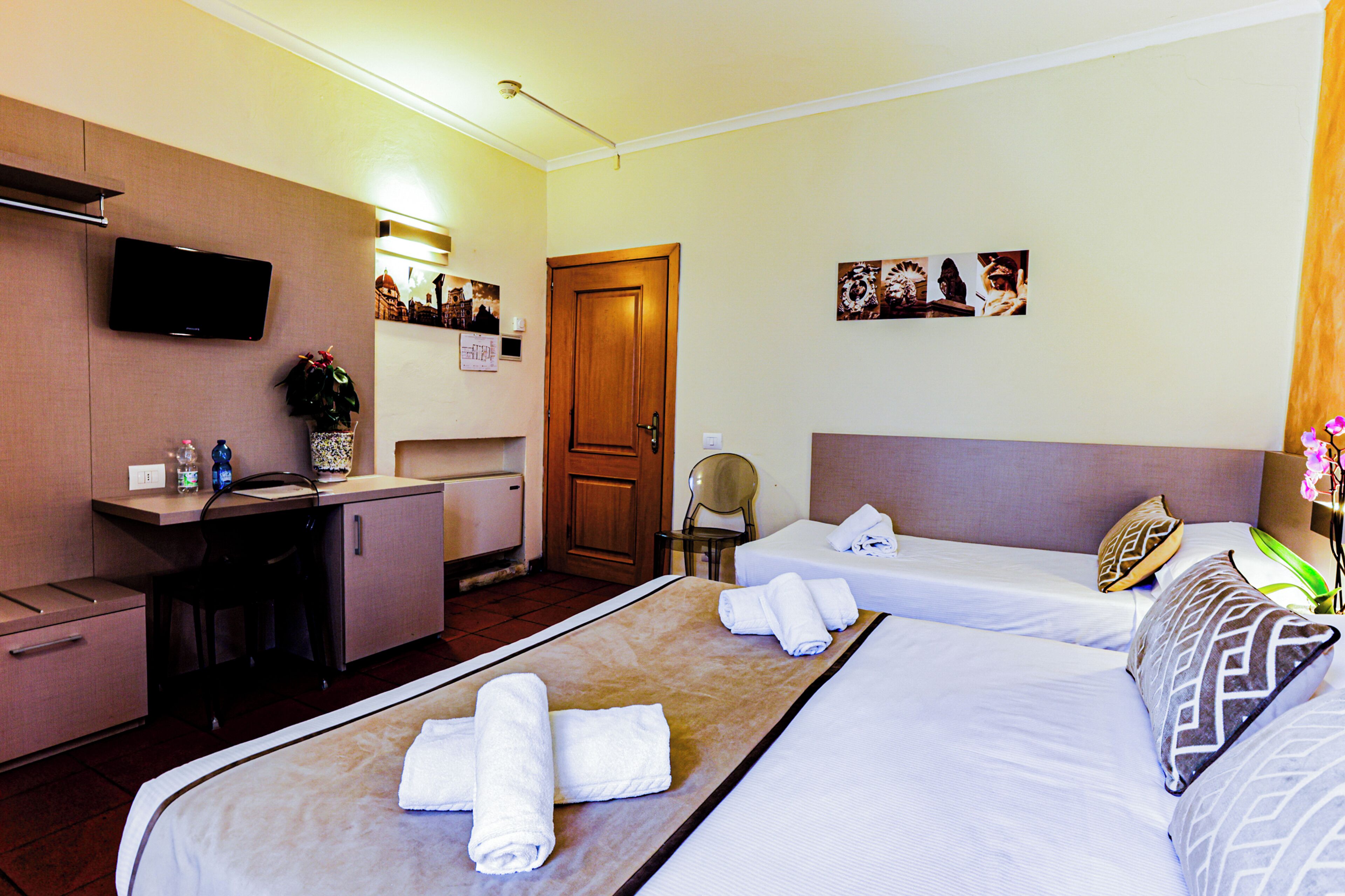 A hotel room with two beds, a desk, a TV, and a door.