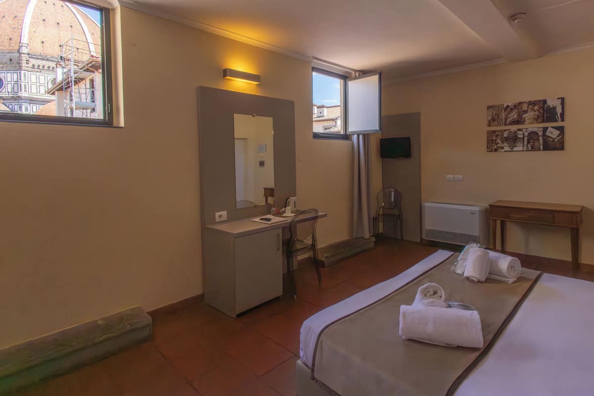 Une chambre d’hôtel équipée d’un lit, d’un bureau, d’une chaise, d’une fenêtre donnant sur un immeuble et d’un téléviseur fixé au mur.