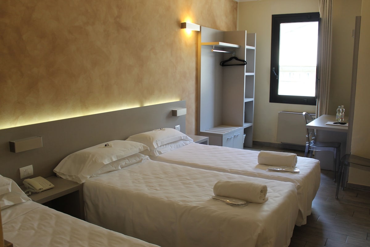Une chambre d’hôtel avec deux lits, un bureau, une chaise, un porte-manteau et une fenêtre.