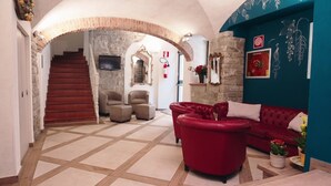 A spacious living area with a red leather sofa, a stone fireplace, and a staircase leading to another level. - Albergo Firenze (Florence)