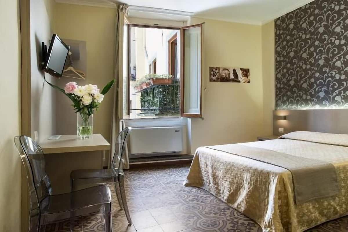 Une chambre d’hôtel équipée d’un lit, d’un bureau, d’une chaise et d’une fenêtre donnant sur un paysage verdoyant.