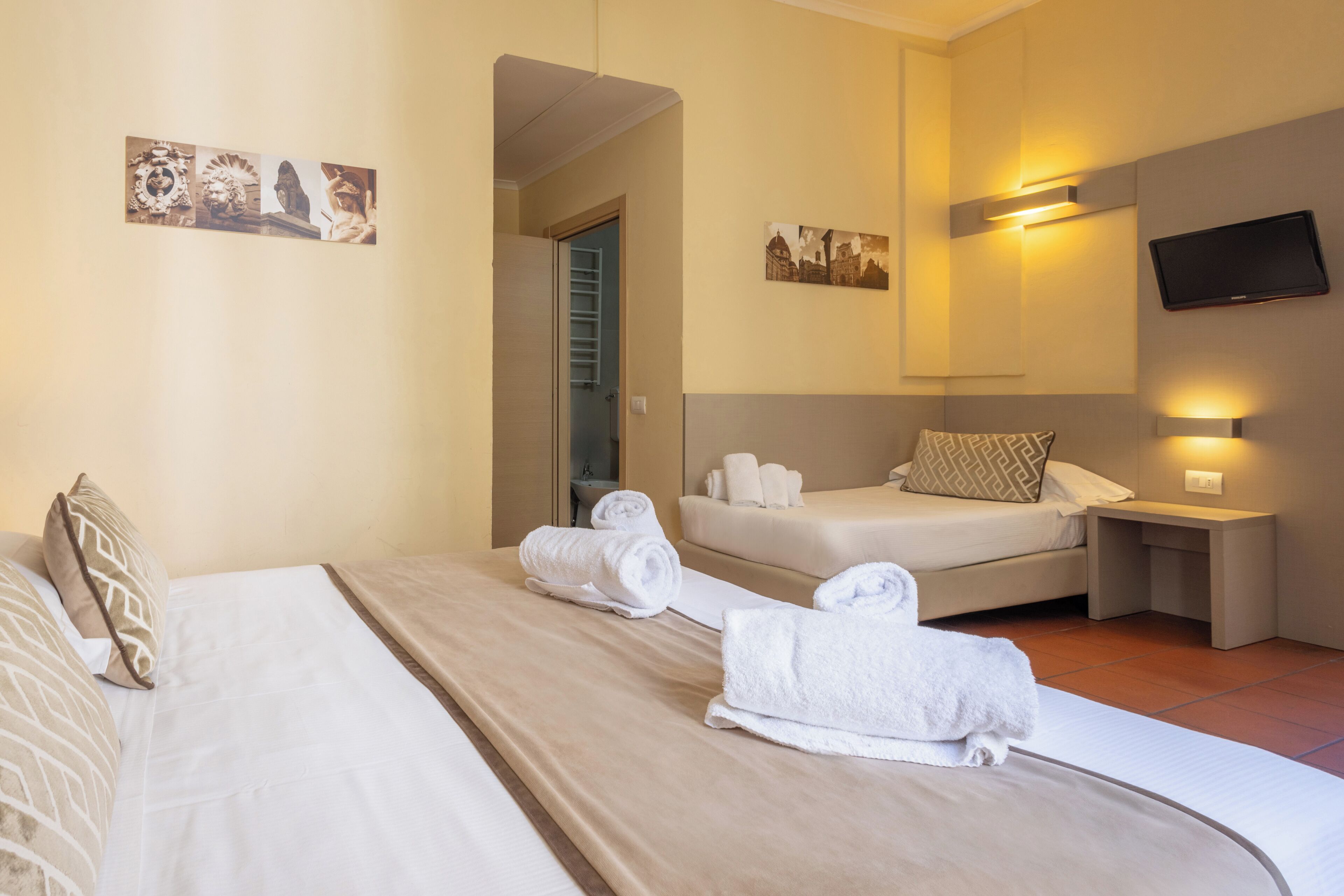 Une chambre d’hôtel avec deux lits, une télévision et une salle de bain visible à travers une porte ouverte.