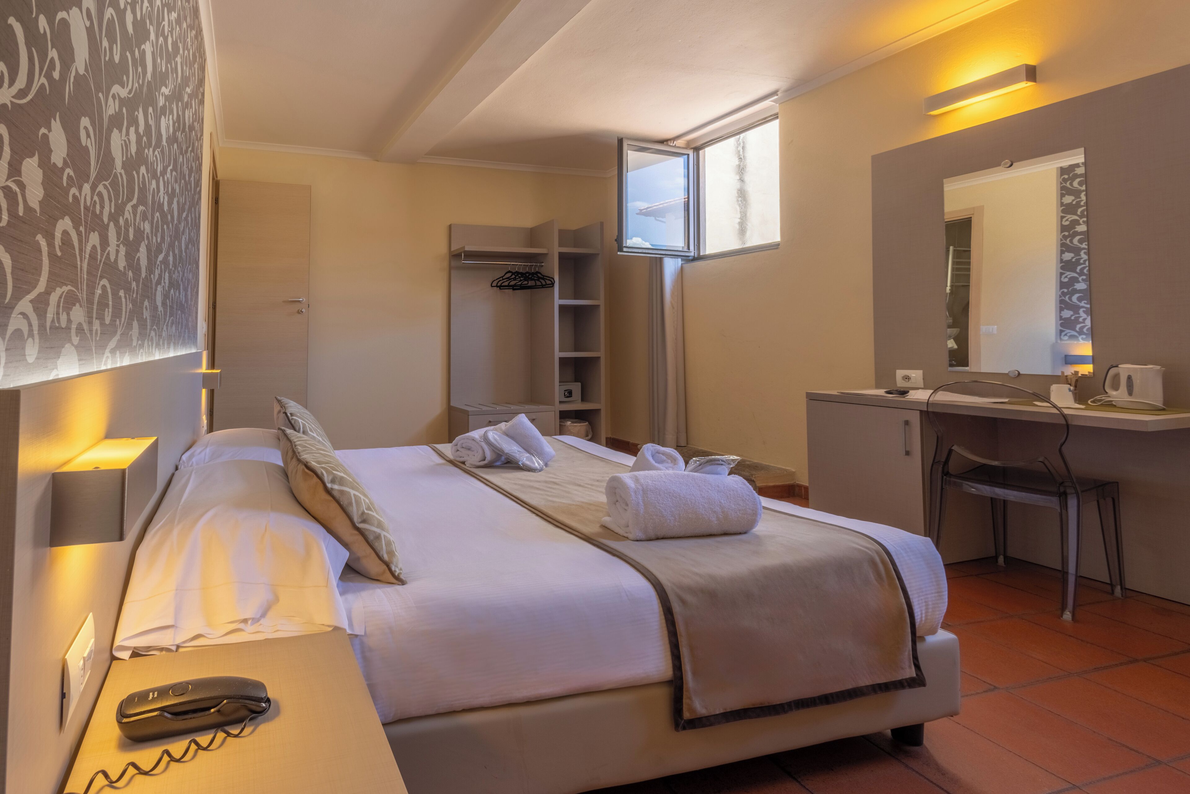 A hotel room with a bed, bedside table, desk, chair, and a window.
