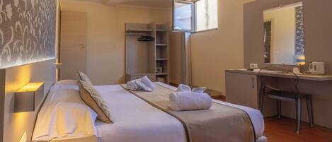 A hotel room with a bed, bedside table, desk, chair, and a window.
