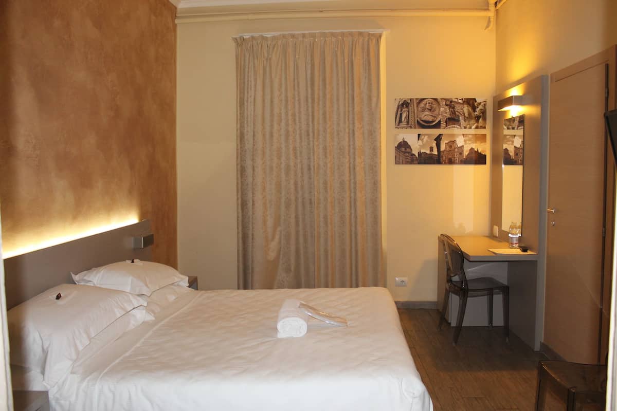 Une chambre d’hôtel avec un lit, un bureau, une chaise et un rideau.