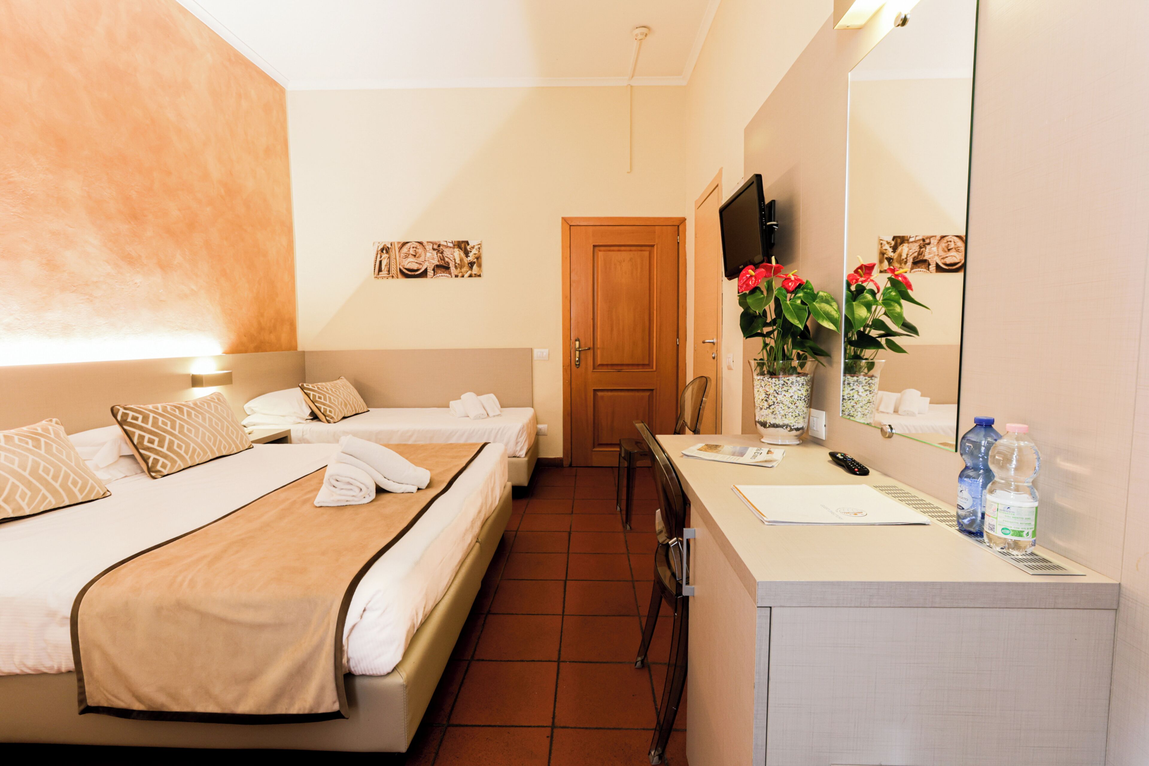 A hotel room with two beds, a desk, a chair, a mirror, and a door.