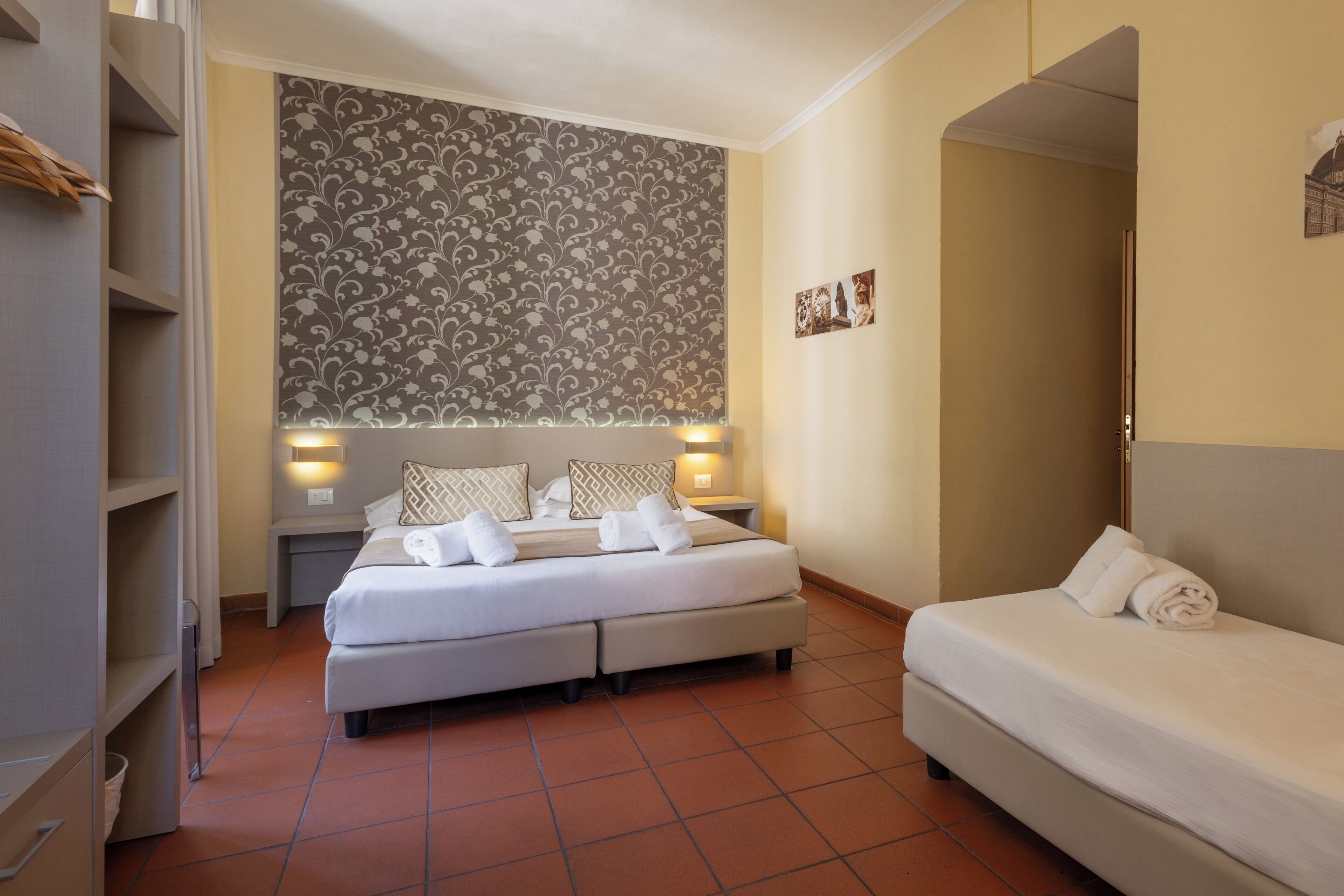Ein Hotelzimmer mit einem Bett, einem Sofa, einem Nachttisch und einer Wand mit ornamentalem Wandpapier.